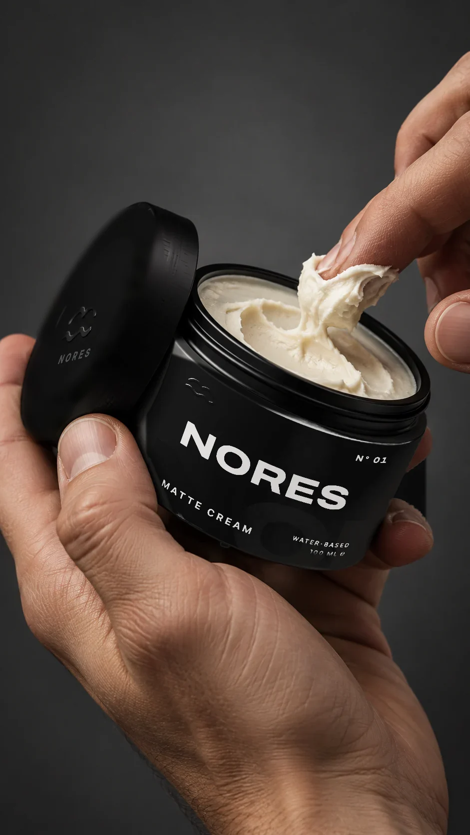 A barber's hand taking cream from an open NORES jar